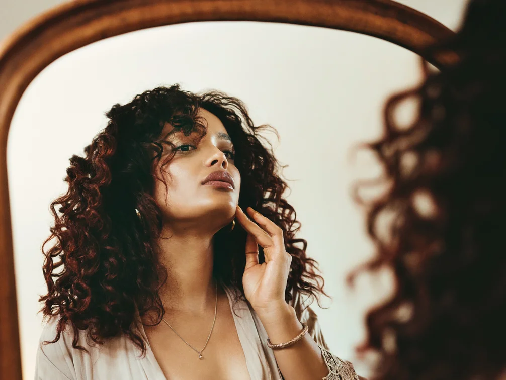 Curly haired woman looking in the mirror at her face